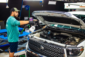 A person using The Rag Company Ultra Air Engine Blaster to clean the engine of their white truck.