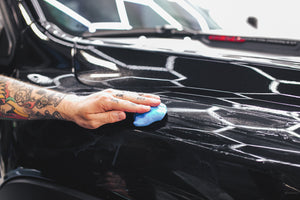 A hand using The Rag Company Clay Bar on a black truck.