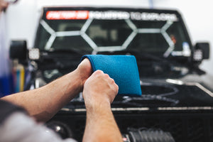 A person putting on a blue Ultra Clay Mitt in front of a black jeep.