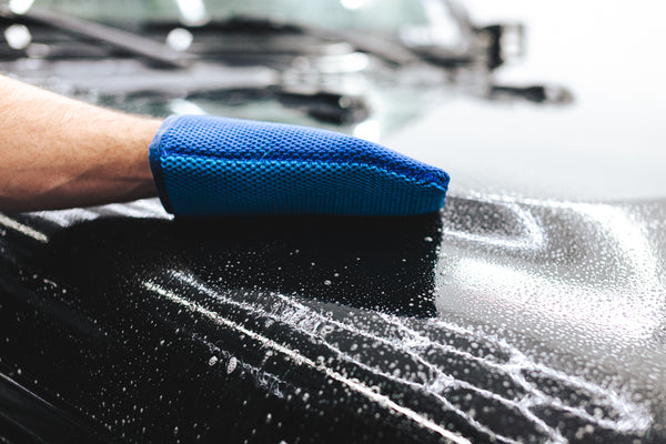 A person wiping a black Jeep Gladiator with a blue Ultra Clay Mitt. 