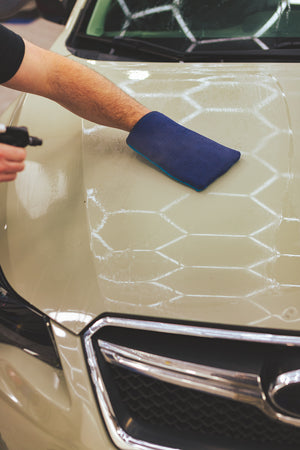 A person scrubbing the hood of a tan car with a blue Ultra Clay Mitt.