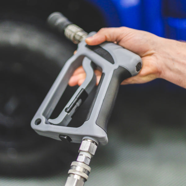 A person holding a TRC Ultra H2O Spray Gun connected to a pressure washer hose.