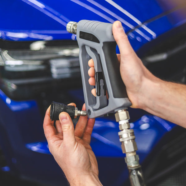 A close up of a TRC Ultra H2O Spray Nozzle being placed into the holder on a TRC Ultra H2O Spray Gun with a blurry blue car in the background.