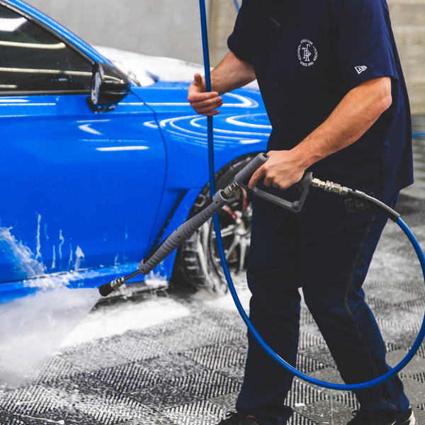 A person spraying water onto a blue car using a TRC Ultra H2O Spray Wand.