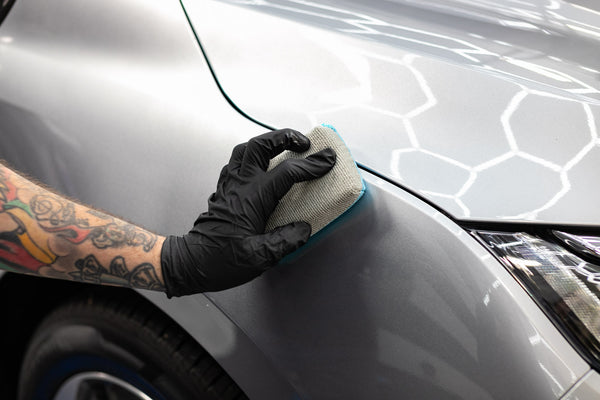 A person using an Ultra Sponge to wipe the hood of a grey vehicle.