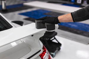 A person wearing black rubber gloves wiping a white Porsche gt3 with the Ultra Safe Sponge. 