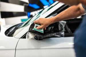 A person using a squeegee to place vinyl on a car's side mirror.