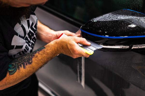 A person using the Yellowtool squeegee to place vinyl on the side mirror.