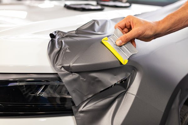 A person using the Yellowtool squeegee to lay vinyl on the exterior of a car.