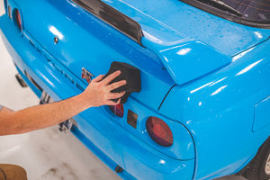 A person scrubbing the back of a blue car with an Ultra Black Sponge.