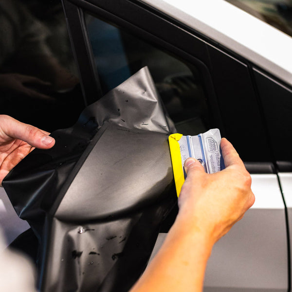 A person using the Yellotools Squeegee to lay vinyl on a car's side mirror. 