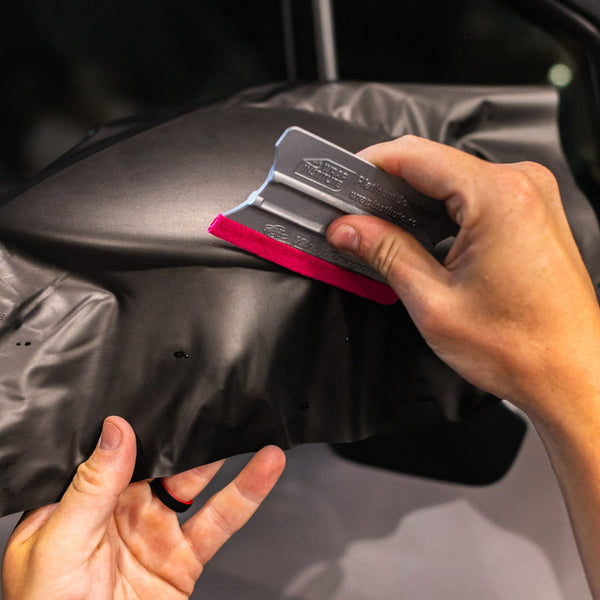 A person laying vinyl on a car's side mirror with a red yellowtools Platinum Squeegee.