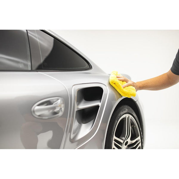 Using a yellow Eagle Edgeless 500 microfiber towel from The Rag Company to wipe down the exterior of a grey Porsche 911 turbo.