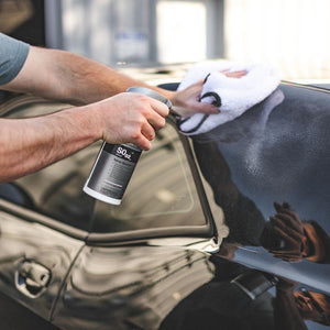 A closeup of a person spraying a window with Koch Chemie Spray Sealant and wiping it with a white towel.