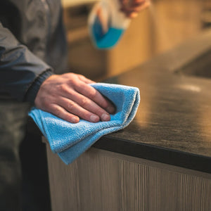A closeup of someone wiping a counter with a blue Premium Terry towel.