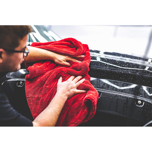 A person cleaning the front of a black car with a red 1500 towel.