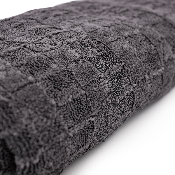 A close-up image of The Gauntlet Towel from The Rag Company. This image is of the unique Gauntlet Grey color and shows the patented alternating twist loop and flare loop weave patterns that increases absorption and softness. These towels are Ice Grey on One side and Gauntlet Grey on the other with a scratcheless suede edge banding them together